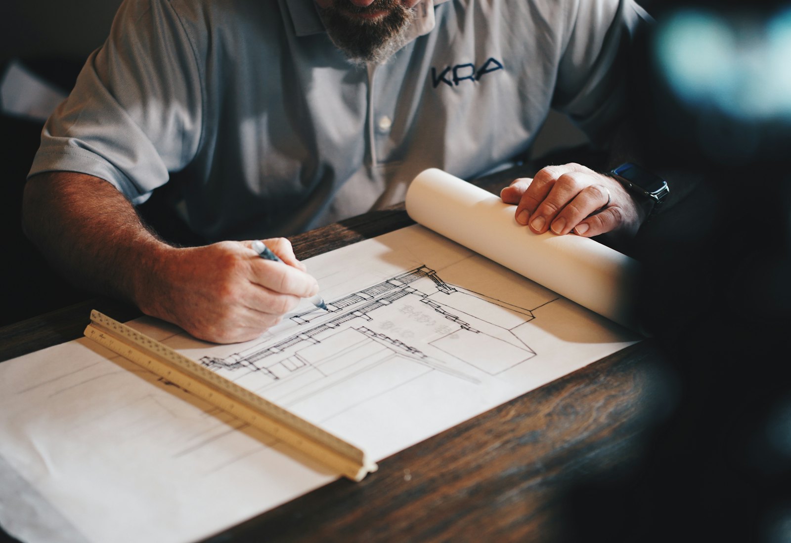 Architectural drawings spread on a desk with a scale ruler and pencil