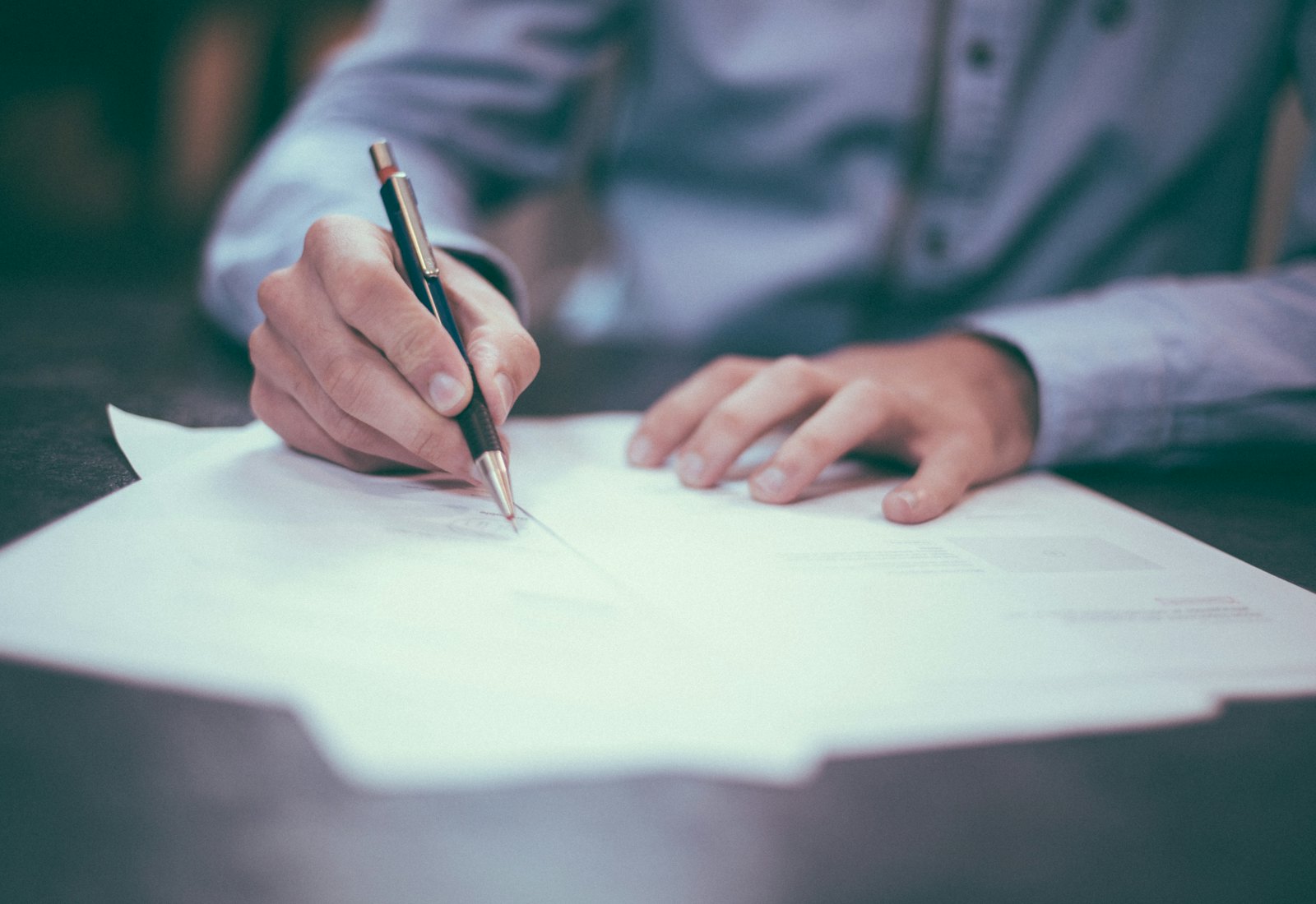 Close view of hands reviewing a printed agreement and a pen on a wooden table